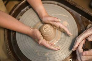 Potter girl works on potter's wheel, making ceramic pot out of clay in pottery workshop photo
