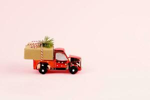 Red toy car delivering Christmas or New Year gift present box on pink background. photo