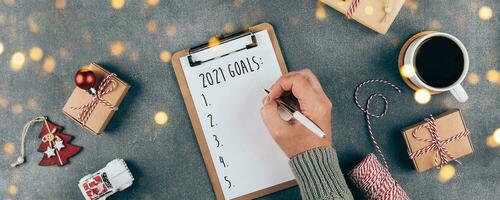 Happy New Year 2021. Woman's hand writing 2021 Goals in notebook. Top view, flat lay. Banner photo