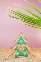 Wooden Christmas tree with sparkles in the sand with a palm tree on a pink background. Holidays in hot countries. Vertical. Copy space photo