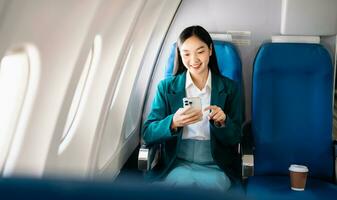 Attractive Asian female passenger of airplane sitting in comfortable seat while working laptop and tablet with mock up area using wireless connection. Travel in style, work with grace. photo