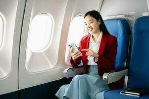 Attractive Asian female passenger of airplane sitting in comfortable seat while working laptop and tablet with mock up area using wireless connection. Travel in style, work with grace. photo