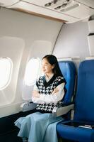 Attractive Asian female passenger of airplane sitting in comfortable seat while working laptop and tablet with mock up area using wireless connection. Travel in style, work with grace. photo