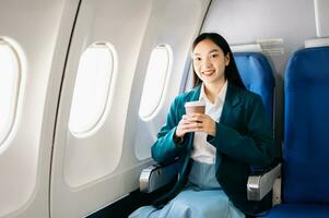 retrato de exitoso asiático mujer de negocios o empresario en un formal traje en un avión sentado en negocio clase utilizando un teléfono, computadora ordenador portátil. viaje en estilo, trabajo con gracia. foto