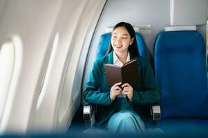 Portrait of  successful Asian businesswoman or entrepreneur in a formal suit on an airplane sitting in business class using a phone, computer laptop. Travel in style, work with grace. photo