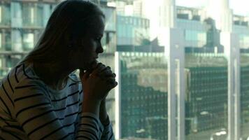 Sad woman being deep in thoughts and then looking out the window with city view video