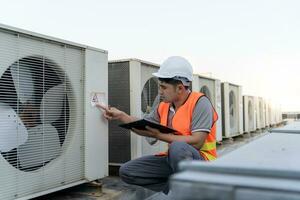 asiático mantenimiento ingeniero trabajos en el techo de fábrica. contratista inspeccionar compresor sistema y planes instalación de aire condición sistemas en construcción. Lista de Verificación, inspector, controlar foto