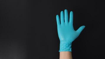 Hand wearing blue medical gloves doing five fingers number on black background. photo