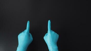 dos mano es vestir azul médico guantes y punto el dedo en negro antecedentes. foto