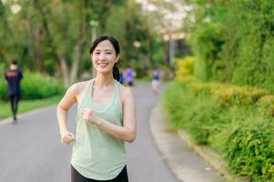 Fit Asian young woman jogging in park smiling happy running and enjoying a healthy outdoor lifestyle. Female jogger. Fitness runner girl in public park. healthy lifestyle and wellness being concept photo