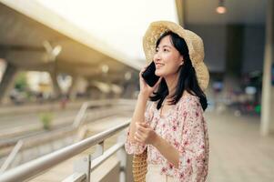 Asian young woman traveler with weaving basket using a mobile phone beside railway train station in Bangkok. Journey trip lifestyle, world travel explorer or Asia summer tourism concept. photo