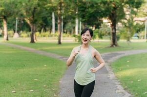 Fit young Asian woman jogging in park smiling happy running and enjoying a healthy outdoor lifestyle. Female jogger. Fitness runner girl in public park. healthy lifestyle and wellness being concept photo