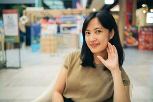 Smiling beautiful asian woman sitting in cafeteria at shopping mall. photo