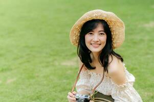 Portrait of asian young woman traveler with weaving hat and basket and a camera on green public park nature background. Journey trip lifestyle, world travel explorer or Asia summer tourism concept. photo