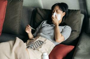 Sick asian woman reading clinical thermometer while cough on a sofa bed at home. photo