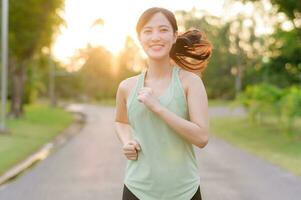 ajuste asiático joven mujer trotar en parque sonriente contento corriendo y disfrutando un sano al aire libre estilo de vida. hembra persona que practica jogging. aptitud corredor niña en público parque. sano estilo de vida y bienestar siendo concepto foto