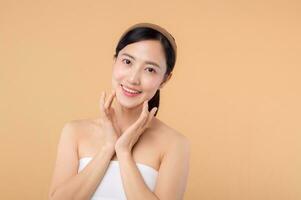 Beautiful girl asian model touching fresh glowing hydrated facial skin on beige background closeup. Beauty face young woman with natural makeup and healthy skin portrait. Skin care concept photo