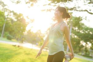 hembra persona que practica jogging. ajuste joven asiático mujer con verde ropa de deporte extensión músculo en parque antes de corriendo y disfrutando un sano exterior. aptitud corredor niña en público parque. bienestar siendo concepto foto