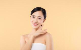 Beautiful girl asian model touching fresh glowing hydrated facial skin on beige background closeup. Beauty face young woman with natural makeup and healthy skin portrait. Skin care concept photo