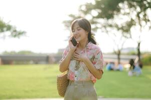 Portrait of asian young woman traveler with weaving basket, mobile phone on green public park background. Journey trip lifestyle, world travel explorer or Asia summer tourism concept. photo