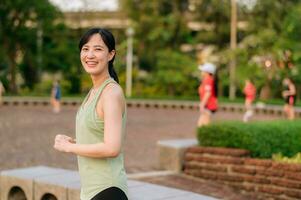 Female jogger. Fit young Asian woman with green sportswear aerobics dance exercise in park and enjoying a healthy outdoor. Fitness runner girl in public park. Wellness being concept photo