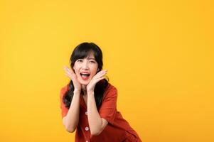 Portrait young beautiful asian woman happy smile dressed in orange clothes looking surprised, reacting amazed, raising eyebrows impressed isolated on yellow studio background. photo