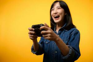 Portrait young asian woman with happy success smile wearing denim clothes holding joystick controller and playing video game. Fun and relax hobby entertainment lifestyle concept. photo