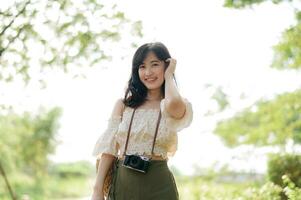 Portrait of asian young woman traveler with weaving hat and basket and a camera on green public park nature background. Journey trip lifestyle, world travel explorer or Asia summer tourism concept. photo