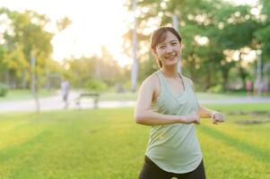 hembra persona que practica jogging. ajuste joven asiático mujer con verde ropa de deporte extensión músculo en parque antes de corriendo y disfrutando un sano exterior. aptitud corredor niña en público parque. bienestar siendo concepto foto