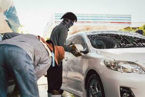 Male worker washing car at car station outdoors with foam and sponge. photo