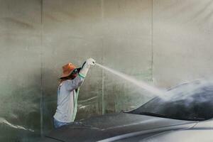 Worker washing auto with high pressure water jet in car wash. photo