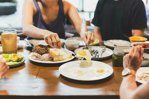 Woman eating fried eggs breakfast with friends on wooden table. photo