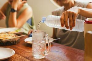 mujer torrencial frío agua desde botella dentro vaso a cena mesa. foto