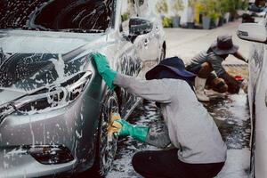 Male worker washing car at car station outdoors with foam and yellow sponge. photo