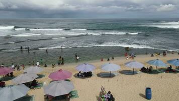Aerial drone view of umbrellas, boats and people having holiday at the beach in Yogyakarta Indonesia video