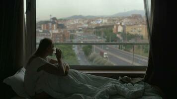 Woman in bed drinking tea and looking at city video