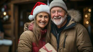 A Happy Senior Couple Holds A Wrapped Christmas Gift Outdoors in a light Snowfall. photo