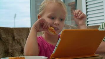 pequeno menina comendo pizza e assistindo desenhos animados video