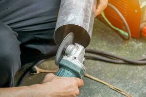 Closeup hands of laborer holding electric angle grinder working cutting galvanized pipe at construction site with sun flare background. photo