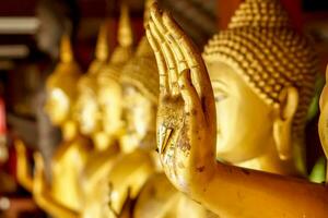 Closeup and crop hand of golden Buddha statue with a gold leaf on blurred golden Buddha statue stand strong line background photo