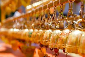 Closeup and perspective view group of small golden bells hang in Thai temple on blurry background. photo