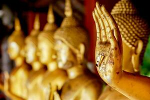 Closeup and crop hand of golden Buddha statue with a gold leaf on blurred golden Buddha statue stand strong line background photo