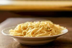 Closeup fried Chinese noodle in white ceramic plate on wooden and blurry background. Thai and Chinese people popular eaten vegan foods in Chinese vegetarian festival in October every years photo