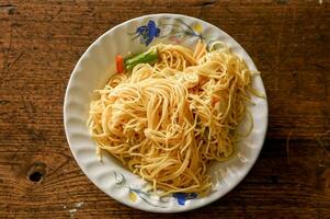 Closeup and top view fried Chinese noodle in white ceramic plate on wooden background. Thai and Chinese people popular eaten vegan foods in Chinese vegetarian festival in October every years photo