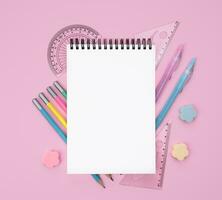 Flatlay composition with blank notepad and school stationery on a pink background. Back to school. Mockup. Top view. Copy space. photo