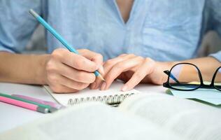 Girl student is preparing for the exam and takes notes in a notebook. Close-up. Selective focus. photo