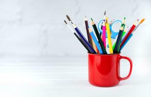 Bright school supplies in a red mug on a white wooden background. Back to school. Banner. Close-up. Place for text. Selective focus. photo