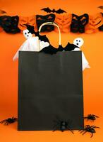 Paper black shopping bag and decor for Halloween on orange bright background. Mock up. Halloween shopping and sale concept. Place for text. Selective focus. photo