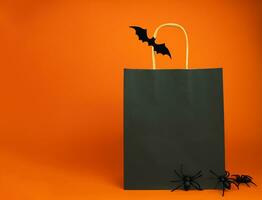 Paper black bag and decor for Halloween on an orange background. Halloween shopping and sale concept. Mock up. Copy space. Selective focus. photo