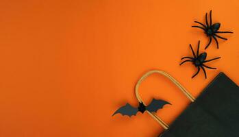 Paper black package, bat and spiders on orange background. Halloween shopping and sale concept. Flatlay composition. Banner. Place for text. photo